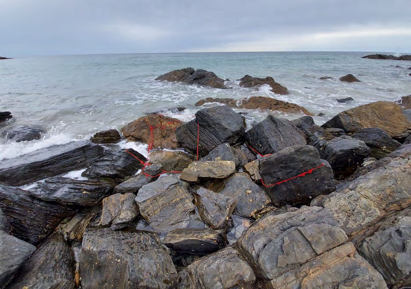 Red yarn stretched across dark rocks at the shoreline