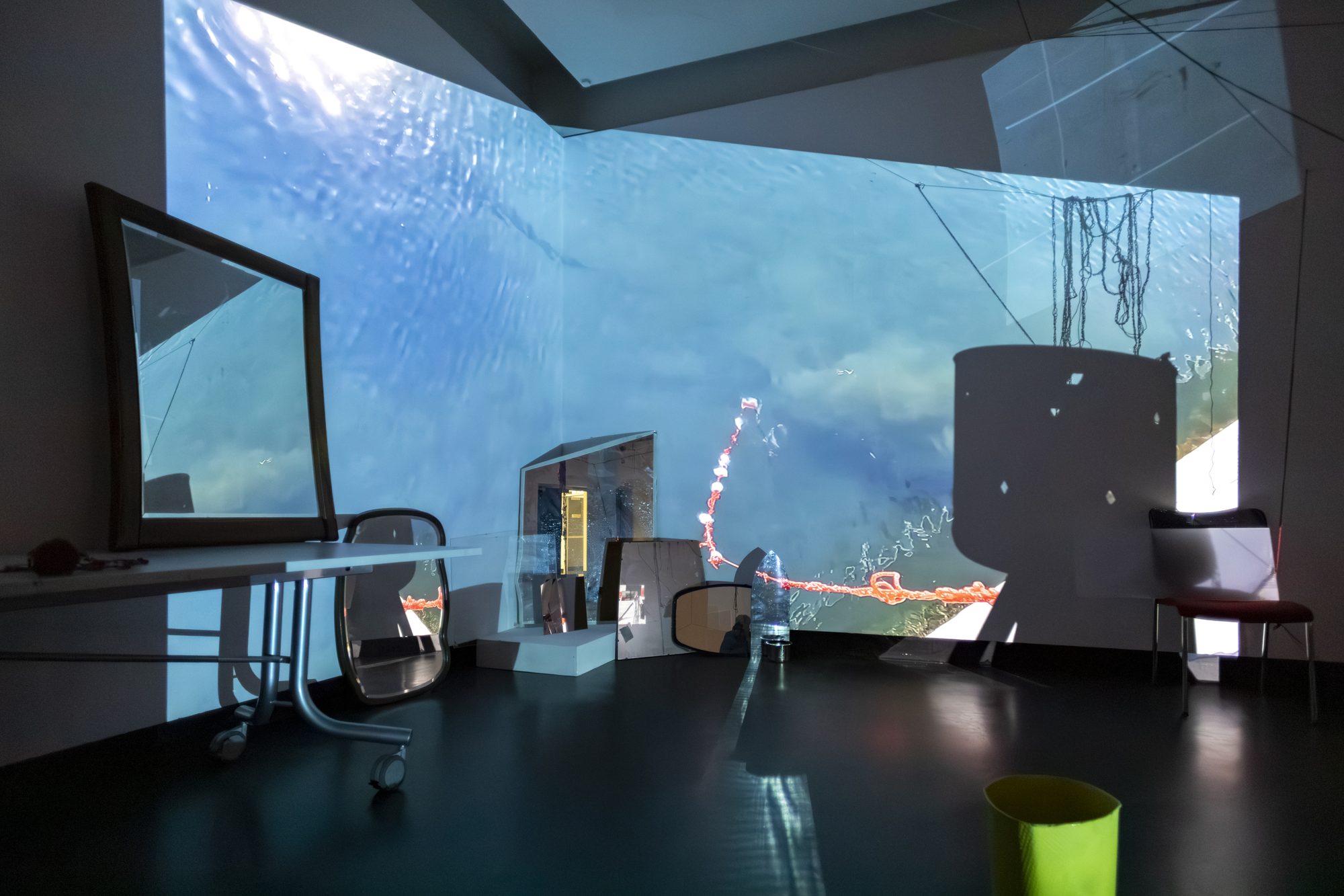 Underwater footage projected across a corner of the gallery, with a mirror and a chair