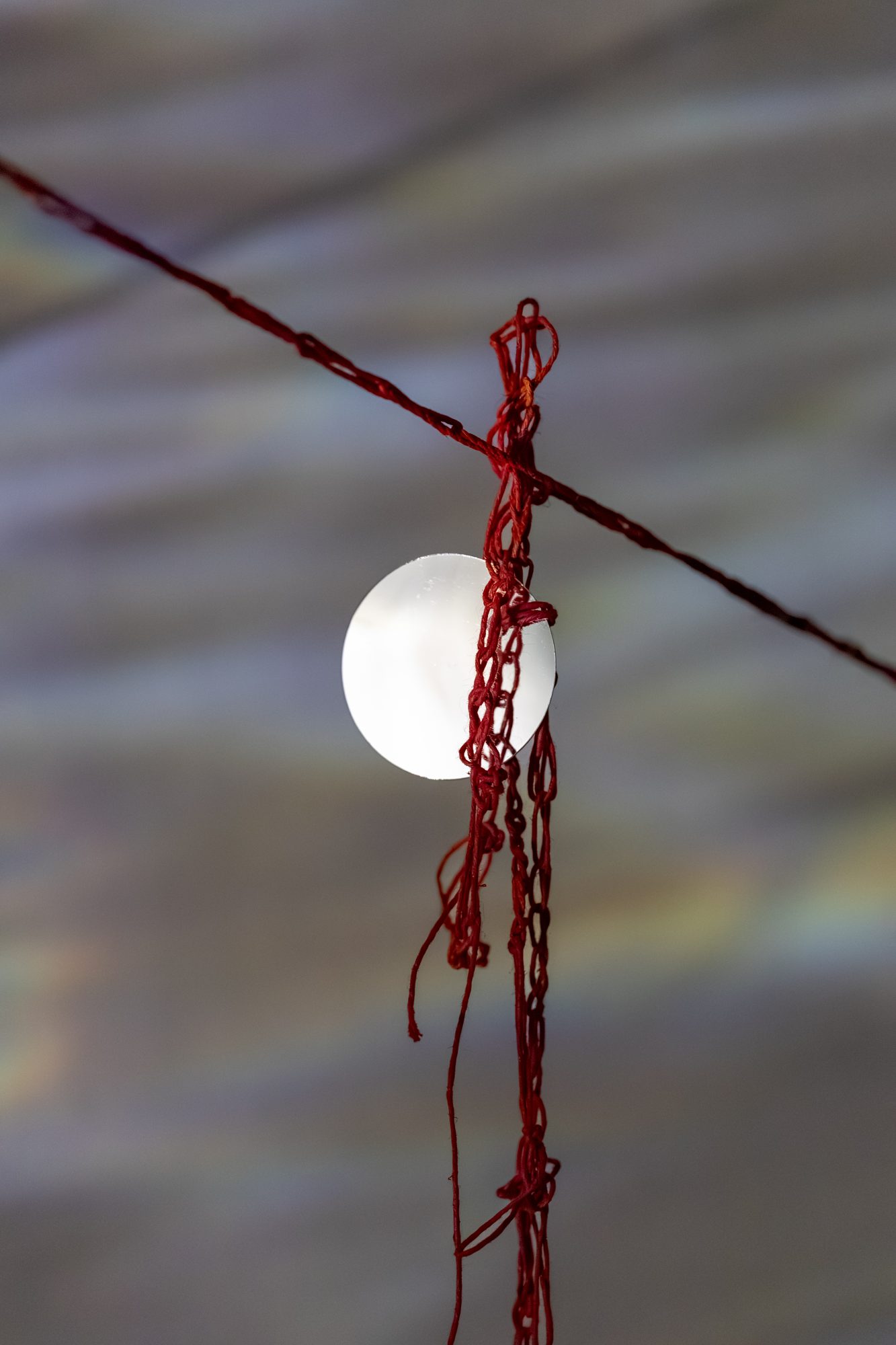 A knotted red yarn hanging on a line in front of a round white light