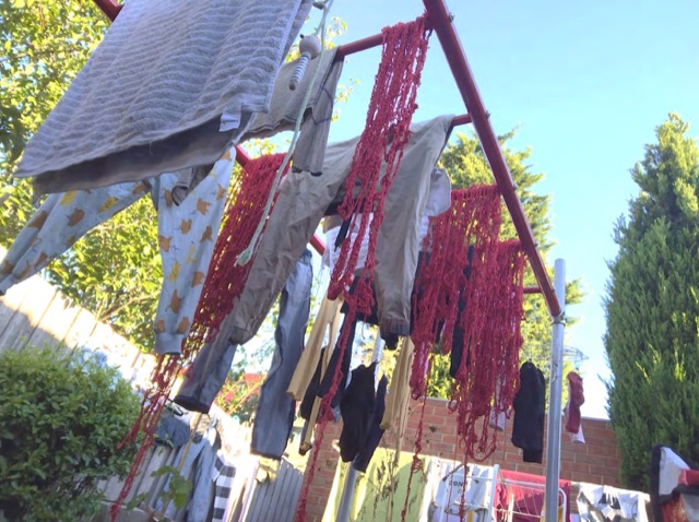 Lengths of red hemp yarn hanging from a clothesline among laundry