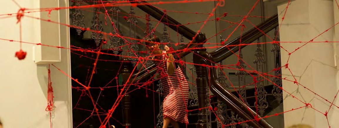 The artist weaving beneath a canopy of red yarn
