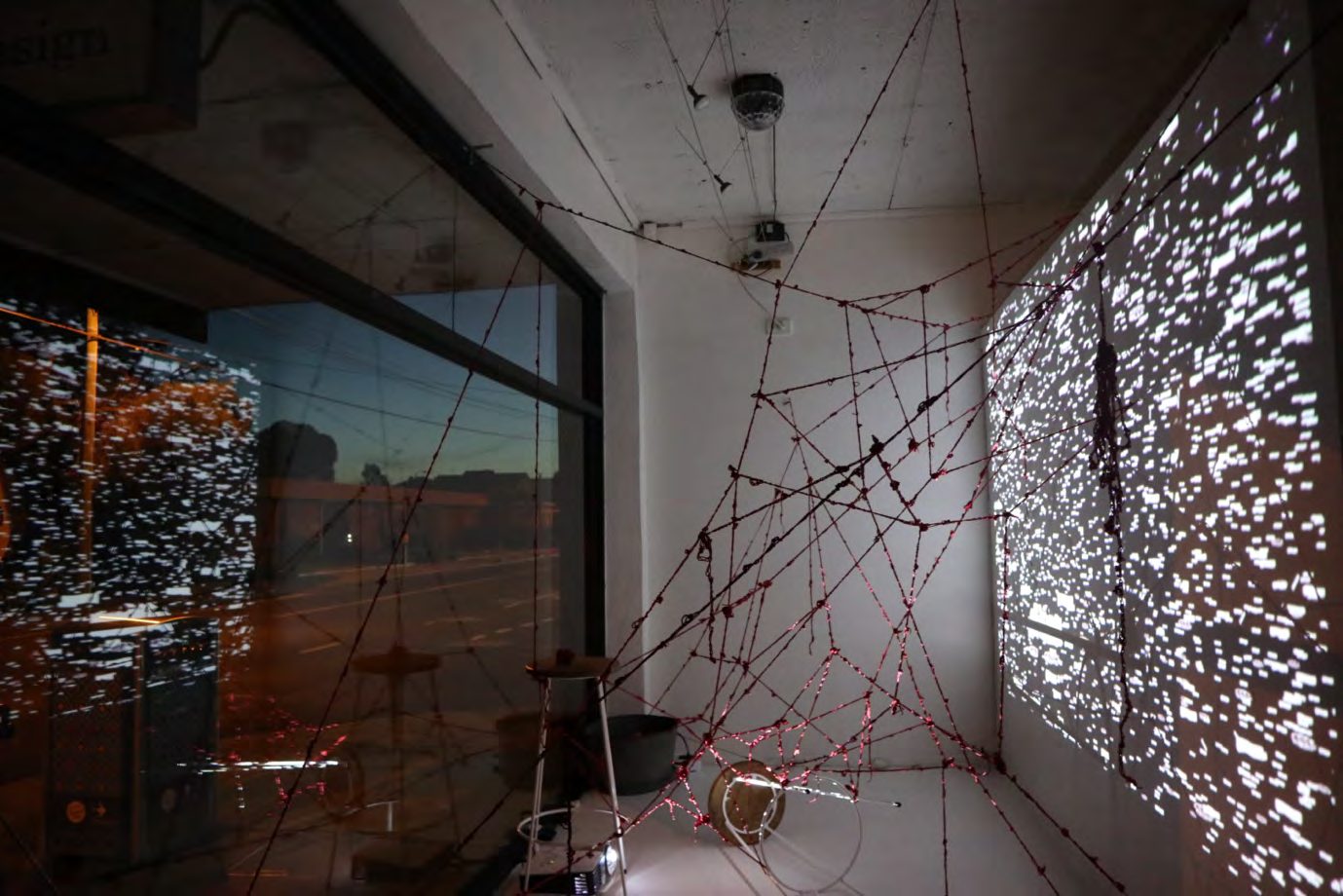Red yarn web inside a room with a patterned screen and night windows