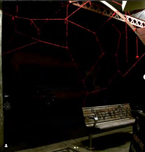 Red yarn lines in darkness above a bench
