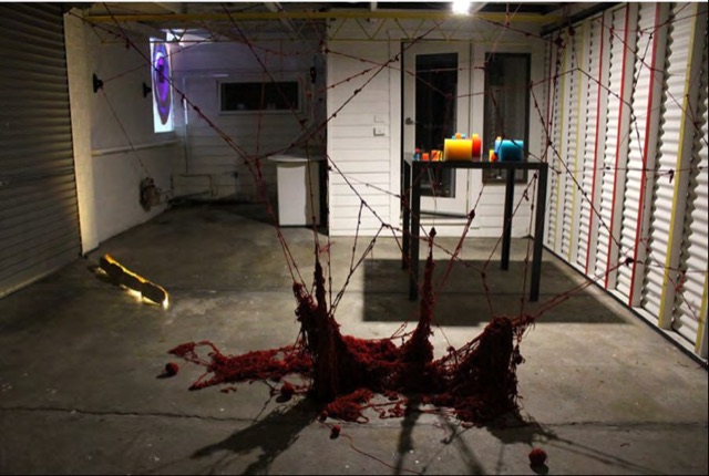 A pool of red yarn on a concrete floor in a white room